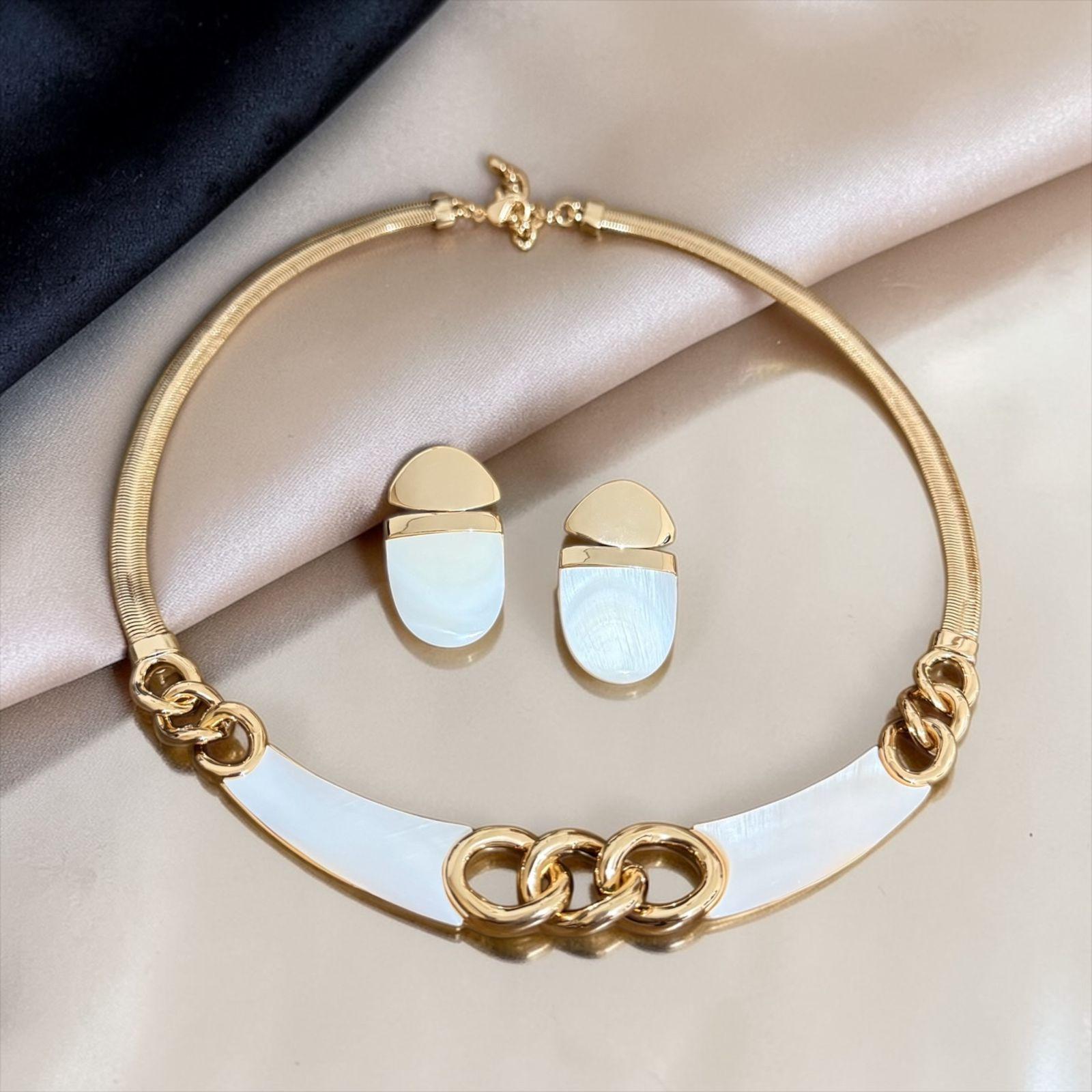 Conjunto Elo Perolado Lux Descrição: Conjunto sofisticado com colar rígido em corrente snake e detalhe central de elos entrelaçados, combinados com acabamento perolado em tom suave que traz leveza e elegância. Acompanha brincos delicados no mesmo estilo, formando uma composição moderna, feminina e refinada para todas as ocasiões.