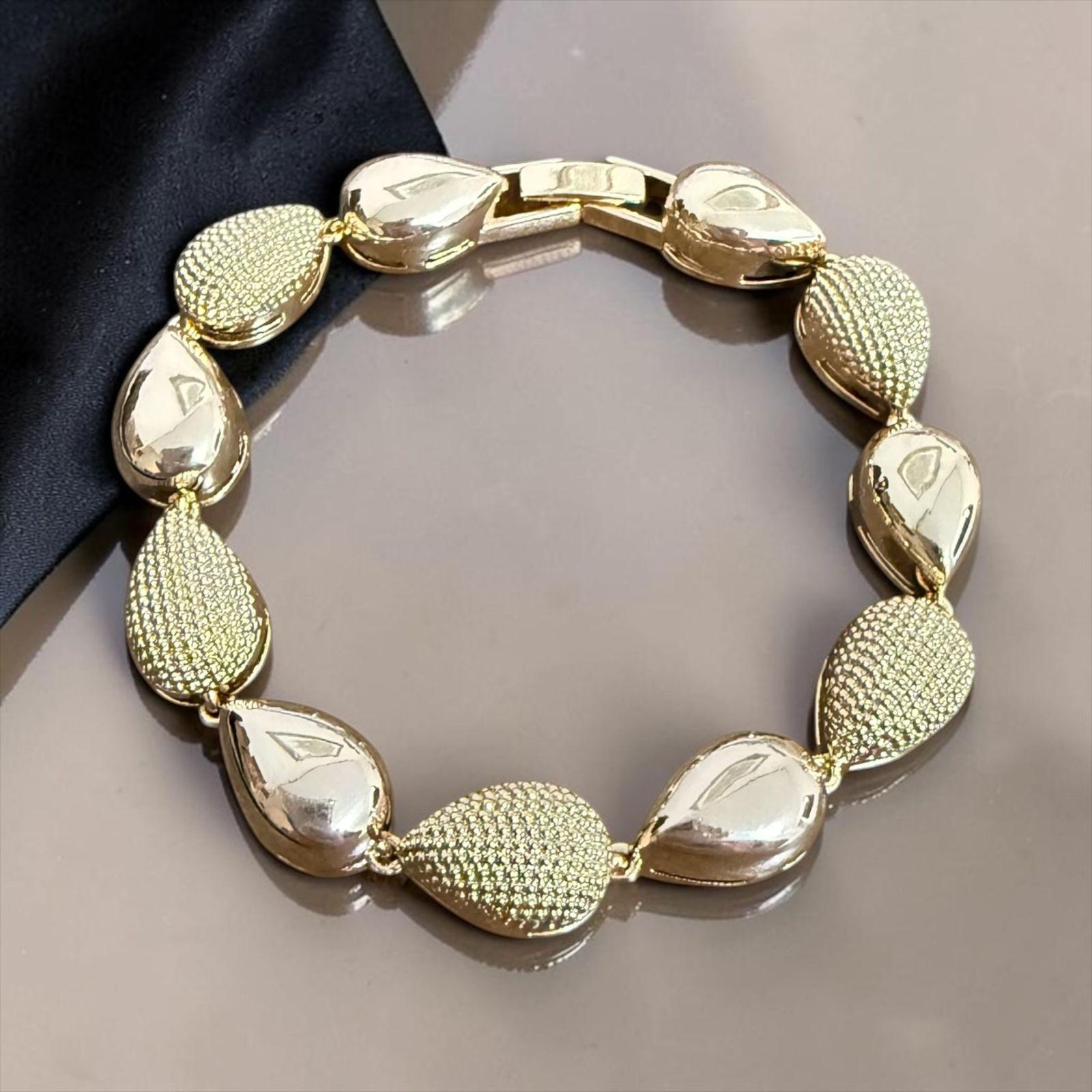 Pulseira Gotas Royale Descrição: Pulseira com design elegante em formato de gotas alternadas, combinando acabamento polido com detalhes texturizados de brilho sofisticado. Uma peça marcante e versátil, perfeita para adicionar requinte e modernidade a qualquer composição.