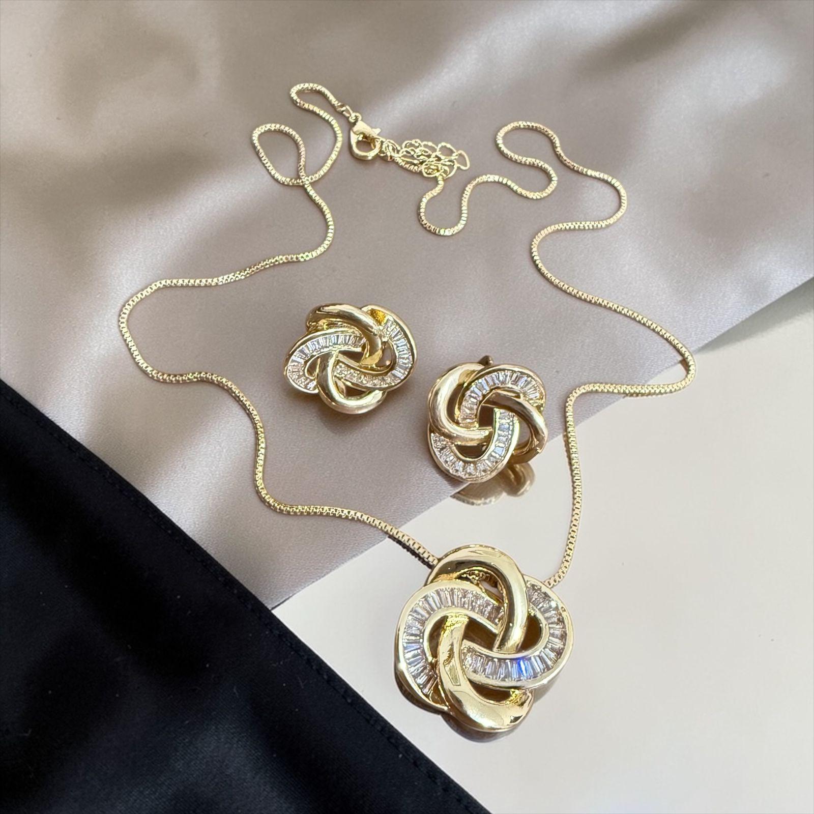 Conjunto Nó Imperial Descrição: Design entrelaçado com acabamento dourado e detalhes em pedras lapidadas que refletem sofisticação e poder. Um conjunto marcante que simboliza conexão, elegância e presença.
