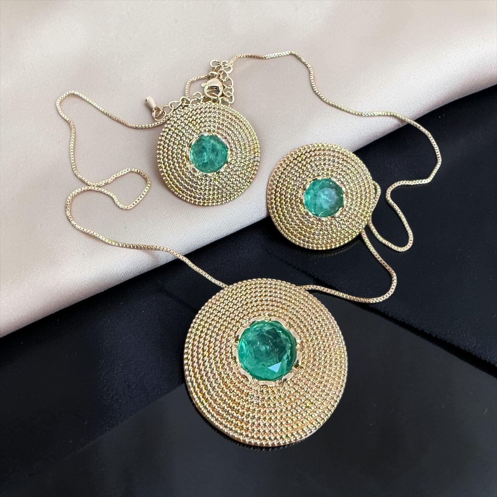 Conjunto Aura Esmeralda Imperial Descrição: Conjunto sofisticado com design circular em alto relevo, ricamente texturizado e finalizado em dourado intenso. O destaque fica por conta da pedra central em tom esmeralda, que transmite elegância, poder e exclusividade. Uma peça imponente, perfeita para mulheres que desejam marcar presença com luxo e personalidade.
