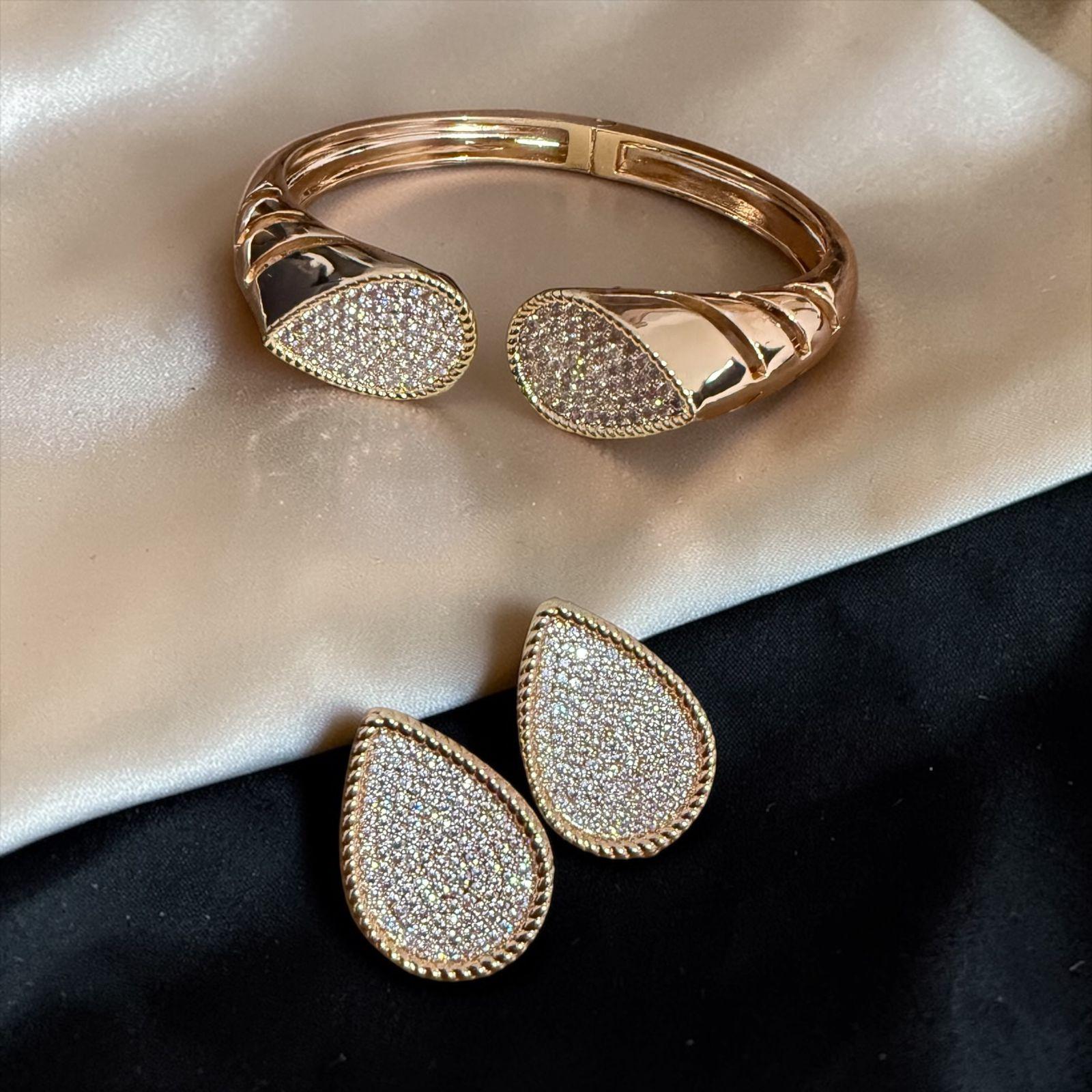 Conjunto Gota Glam Lux Descrição: Conjunto elegante composto por bracelete aberto e brincos em formato de gota, totalmente cravejados em zircônias que proporcionam brilho intenso e sofisticado. O design moderno com acabamento polido traz imponência e delicadeza na medida certa, ideal para elevar qualquer produção com glamour e requinte.